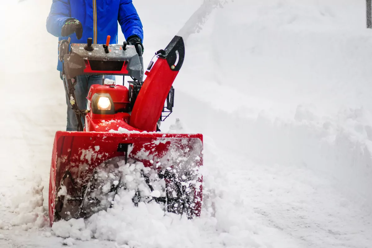 A man with a red snow-covered snow blower clears the area from snow. Clearing the area from snowfall.